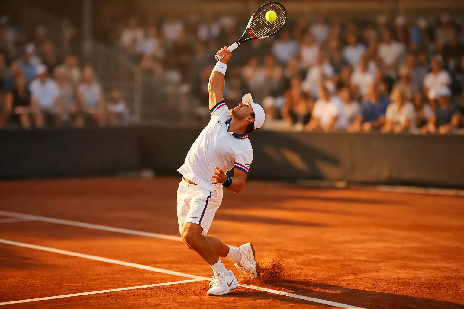 Tenista profesional ejecutando un potente servicio en pista de tierra batida